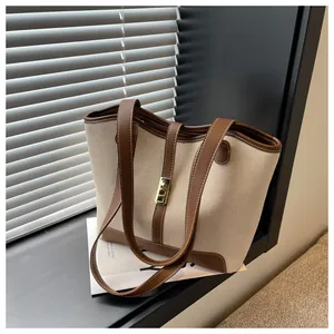 Close-up of beige canvas tote bag with brown leather trim and golden metal lock detail