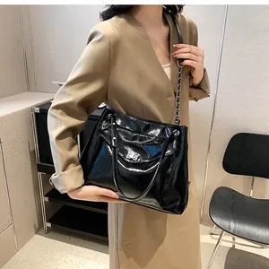 Detail of glossy black patent leather tote bag with silver lock and chain strap