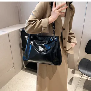 Detail of glossy black leather tote bag with silver metal lock and chain strap