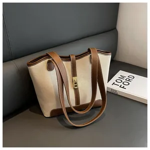 Detail of canvas tote bag featuring contrast leather trim and golden metal buckle closure