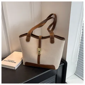 Close-up of cream canvas tote bag with brown leather trim and golden metal lock detail