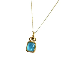 Collier vintage plaqué or avec un pendentif en cristal bleu rectangulaire sur fond blanc