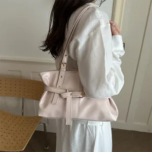 Detail of light pink glossy leather handbag with buckle strap on a model shoulder