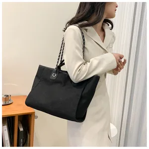 Détail du sac seau en toile noire avec bandoulière chaîne tressée et poignée en cuir chic