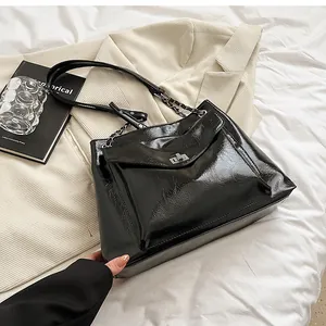 Detail of glossy black patent leather tote bag with silver metal swivel lock and chain strap