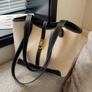 Canvas tote bag with black leather trim and gold lock shown on a modern sofa