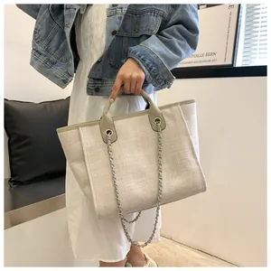 Sac seau tissé beige avec bandoulière chaîne porté par un mannequin en intérieur
