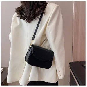 Detail of a black leather crossbody bag on a model wearing an ivory oversized blazer