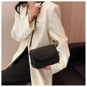 Detailed view of black leather crossbody bag on white suit highlighting size and texture