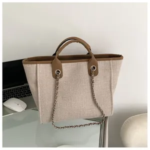 Détail d'un grand sac cabas tissé beige avec bordure marron et chaîne en métal argenté