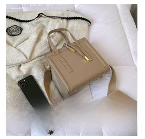 Square khaki crossbody bag with wide strap shown next to phone for size comparison