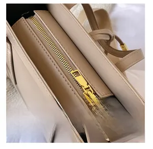 Close-up detail of smooth golden zipper and high-quality beige leather on small square bag