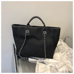 Détail du sac cabas tissé noir avec chaîne argentée et anses en cuir sur un chariot