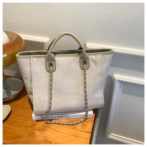 Détail du sac cabas en toile avec garniture en cuir vert et chaîne argentée sur des livres