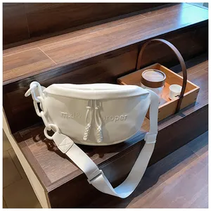 Detail of white PU crescent bag featuring embossed text and thick chain strap on wood