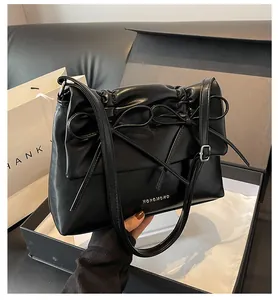 Close-up of black PU leather shoulder bag with bow ties and silver brand logo on gift box