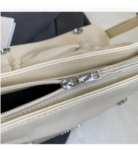 Close-up of smooth metal zipper and rivet detail on the beige soft faux leather handbag
