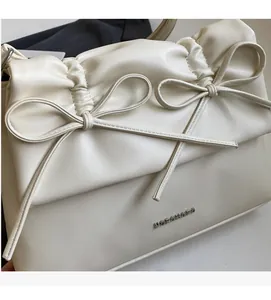 Detailed view of cream leather shoulder bag featuring pleated flap and bow tie accents