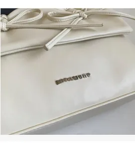 Detail of cream leather bag featuring silver NOROMORO logo and leather bow ornaments