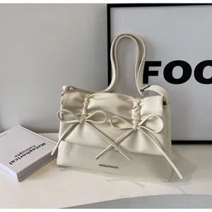 Close-up of cream leather shoulder bag with elegant pleated details and delicate bow accents