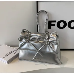 Detail of silver metallic handbag featuring bow decoration and ruched faux leather texture