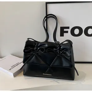 Detail of black faux leather tote bag with elegant double bow and silver logo