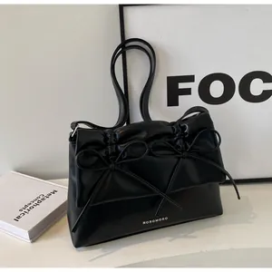 Detail of black leather shoulder bag featuring twin bow accents and a minimalist logo