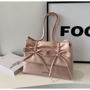 Close-up of soft light pink shoulder bag featuring double bow accents and pleated texture