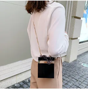 Close-up of black acrylic crossbody box bag with gold metal chain and chunky resin link