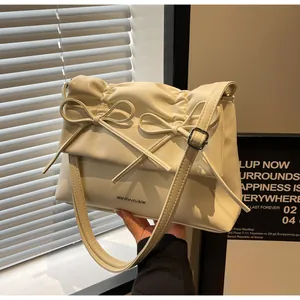 Detail of cream leather shoulder bag featuring decorative bows and pleated flap texture