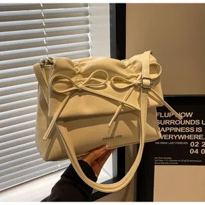 Close-up of cream pleated shoulder bag featuring delicate bow ties and metal logo detail
