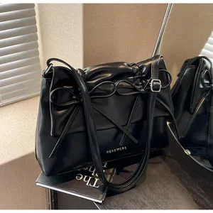Detail of black PU leather shoulder bag with decorative bow and metallic logo