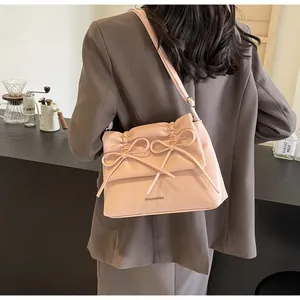 Detail view of pink crossbody bag with decorative bows and pleated flap on model