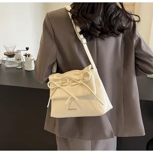 Detailed view of cream-colored crossbody bag with bow accents on a stylish model