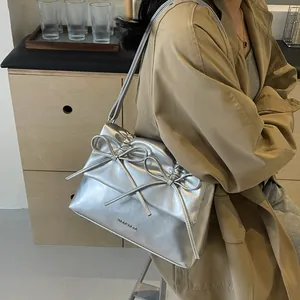 Silver metallic shoulder bag with double bow design and logo detail on beige coat