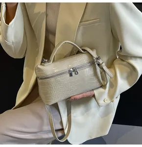 Dettaglio di borsa beige con stampa coccodrillo, doppia zip in metallo e manico superiore