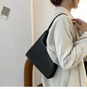 Détail du sac sous le bras en cuir grainé noir porté avec un élégant blazer crème