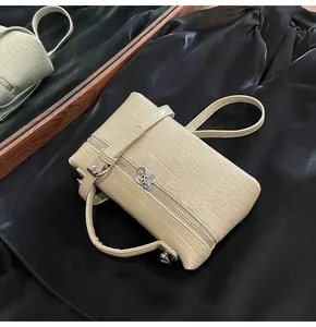 Dettaglio della borsa beige con trama a coccodrillo e cerniere in metallo argentato
