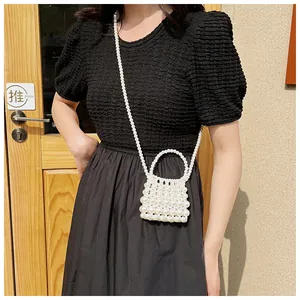 Detail van een handgemaakte witte kralen mini crossbody tas op een zwarte jurk