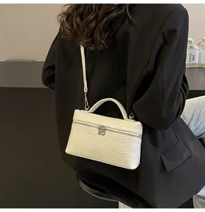 Dettaglio della borsa bianca con motivo a coccodrillo indossata a spalla dal modello