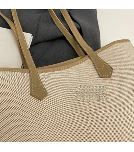 Detailed close-up of precise stitching on beige canvas tote bag with brown leather strap