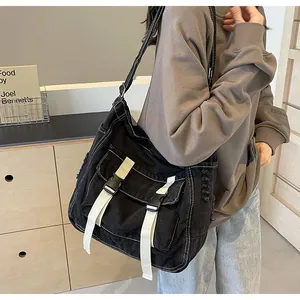 Detail of black canvas messenger bag featuring white buckle straps and distressed edges