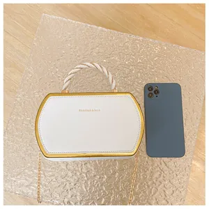 Detailansicht einer weißen sechseckigen Handtasche mit Goldmetallrahmen und Logo