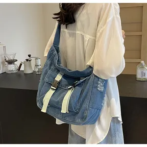 Blue denim messenger bag detail showing frayed edges and white buckle straps