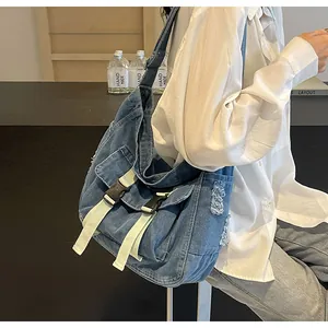 Detail of blue denim messenger bag featuring distressed frayed edges and cream buckled straps