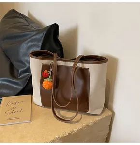 Detail of canvas tote bag with brown leather pocket and handmade orange knit charm