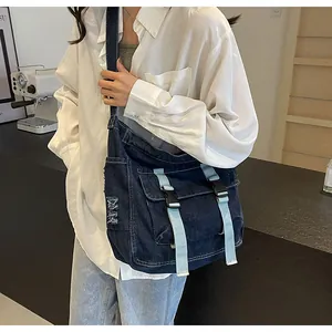 Detail of blue denim messenger bag with distressed texture and buckle straps on a model