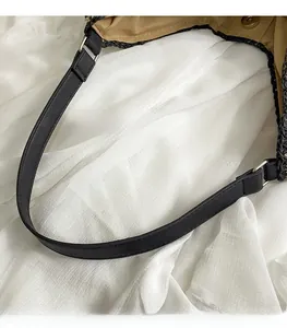 Detail of smooth black leather shoulder strap with silver buckle on woven tote bag
