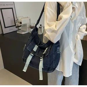 Detail view of dark blue denim messenger bag with raw edges and light blue buckles