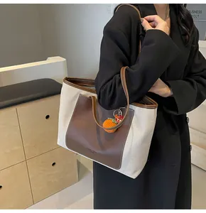 Detail of canvas tote bag with brown leather trim and knitted orange charm accessory